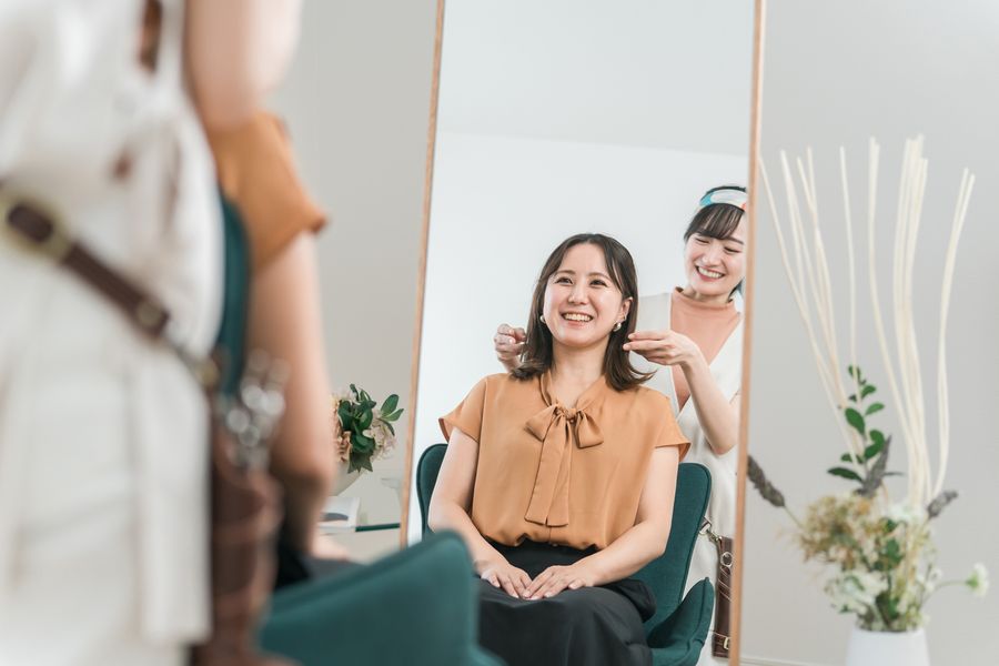 Smiling Asian client in a salon chair talking with her stylist through the mirror