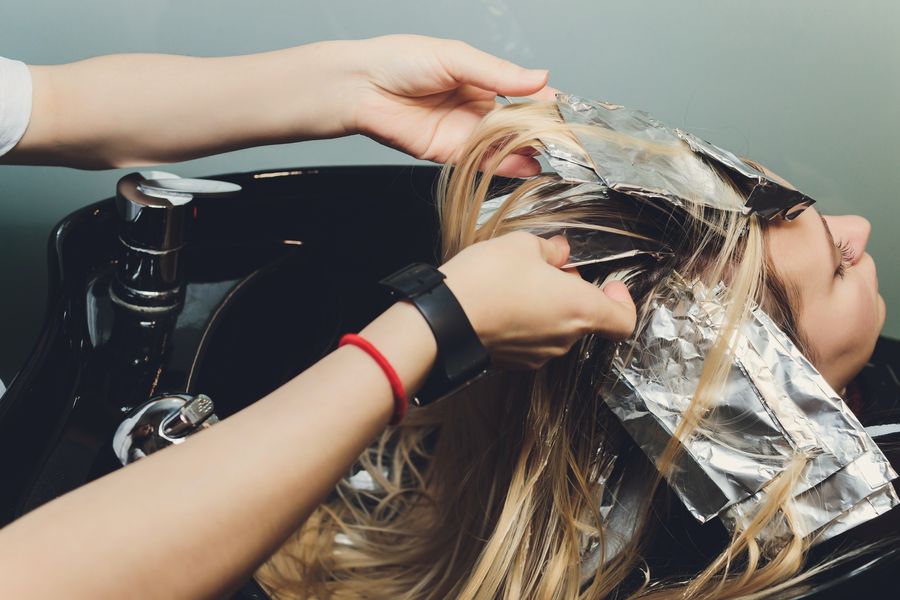 Stylist's hands lifting foiled sections of blonde highlights at the wash bowl