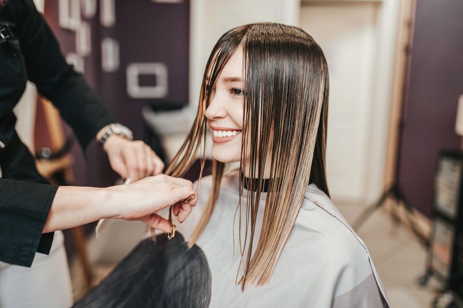 Smiling client with long, sleek, glossy straight hair as her stylist checks the ends
