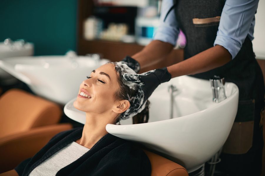 Woman smiling with her eyes closed during a relaxing shampoo at a white wash bowl