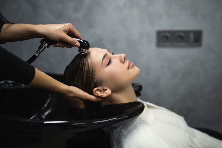 Woman relaxing with her eyes closed as a stylist rinses her long dark hair at the shampoo bowl