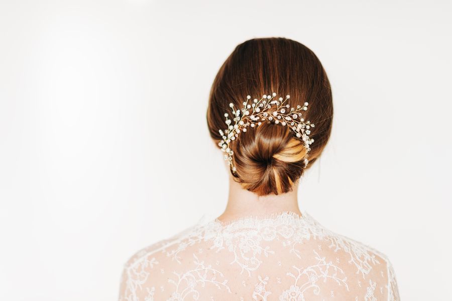 Back view of a bride's low chignon updo with a pearl and crystal hairpiece and lace gown