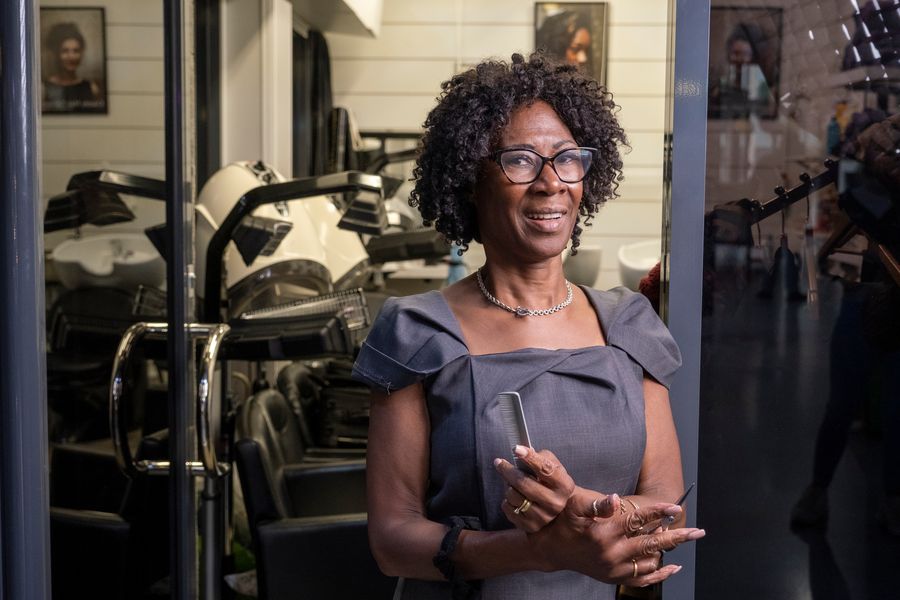 Confident mature Black stylist with natural curls and glasses standing in her salon