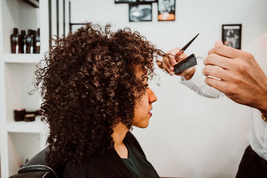 Woman with natural brown curls having her curls shaped by a stylist in a bright salon